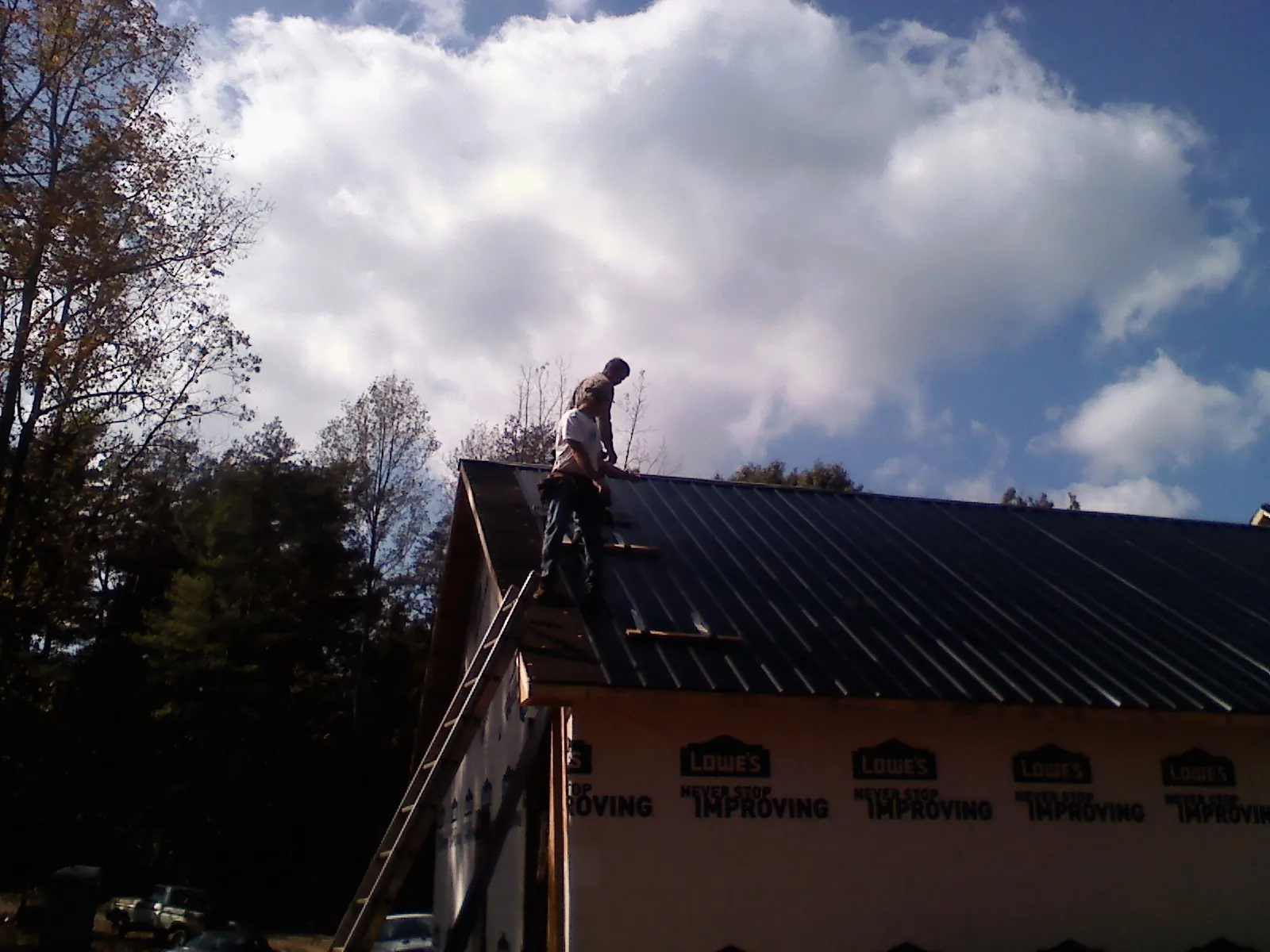 Roofer fastening dark metal panels high against a cloudy sky, from a Roof Inspection job in Republic
