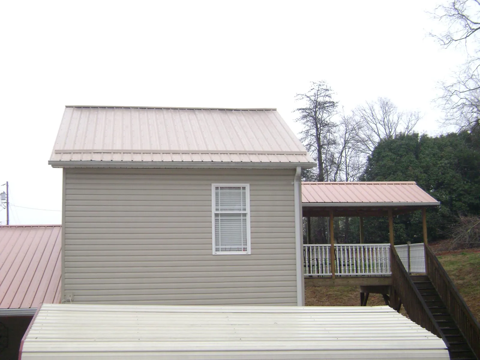 Tan metal roofs on a two story addition and attached porch, from a Roof Replacement job in Republic